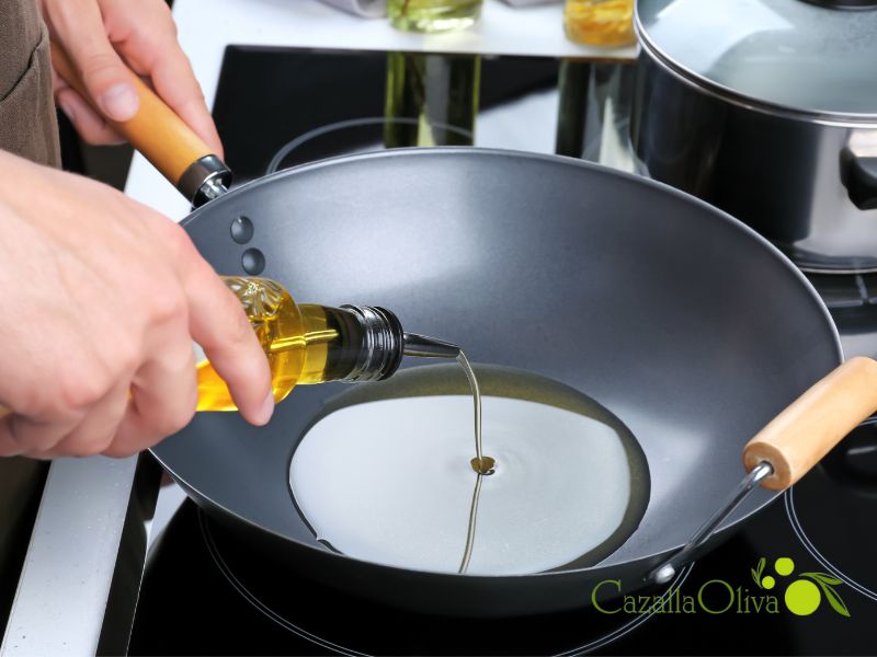 una persona vierte aceite de oliva virgen extra para cocinar en una sarten que esta en una hornilla